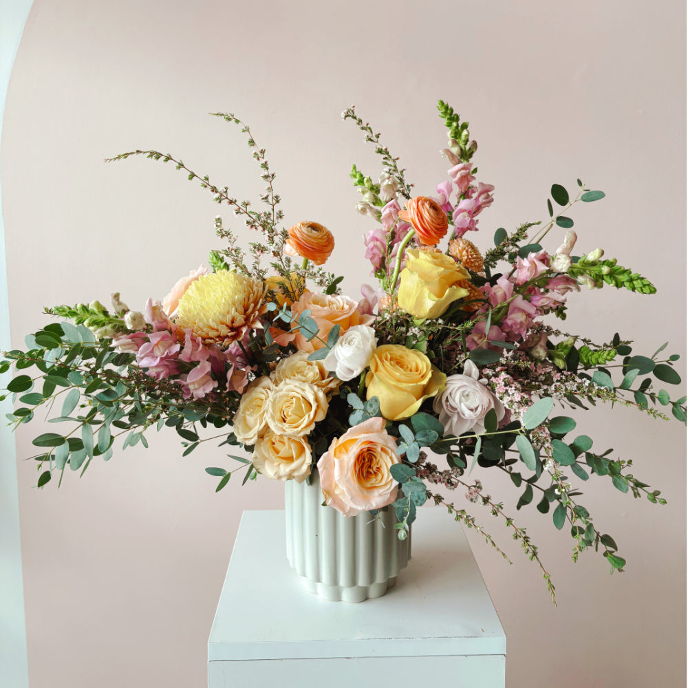 This image shows a large, colorful flower arrangement featuring roses, mums and rununculus