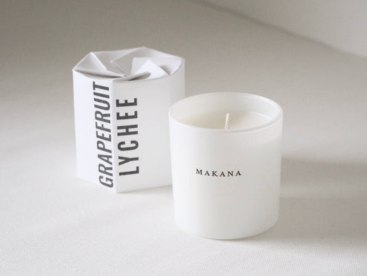 White candle with 'Makana' branding next to a white box labeled 'Grapefruit Lychee'.