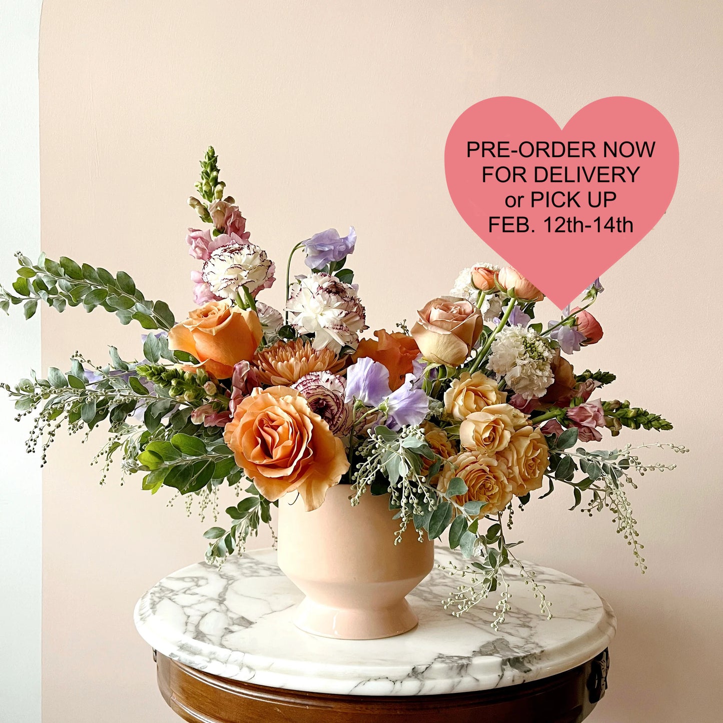 A colorful and bright flower arrangement in a peach vase featuring roses, snapdragons and ranunculus.  Flowers may vary.