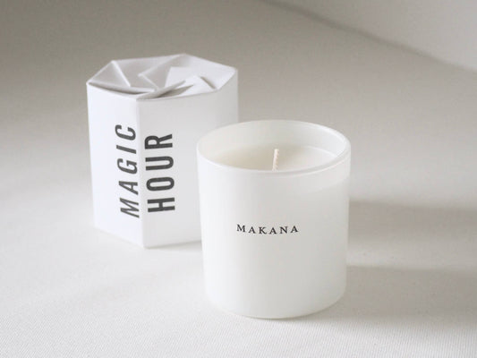 White candle with 'Makana' branding next to a white box labeled 'Magic Hour' on a light background