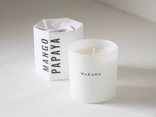 White candle with 'Makana' branding next to a white box labeled 'Mango Papaya'.
