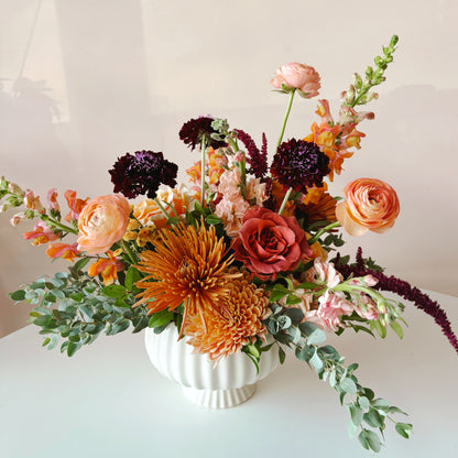 Gather Thanksgiving Centerpiece by Bloomstall featureing a fluted vase, mums, roses, and ranunculus in  fall colors