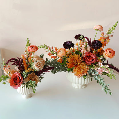 two beautiful, fall colors Thanksgiving flower arrangement featuring roses, ranunculus and stock in a petite pedestal vase.